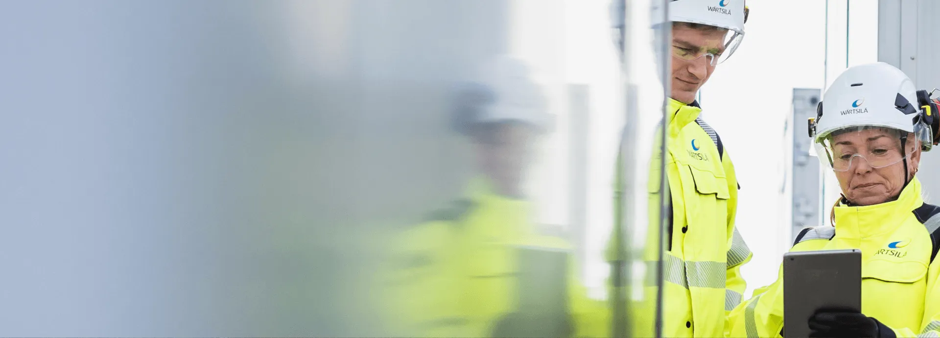 Two Wärtsilä service engineers in high-visibility jackets and hard hats reading a tablet on site