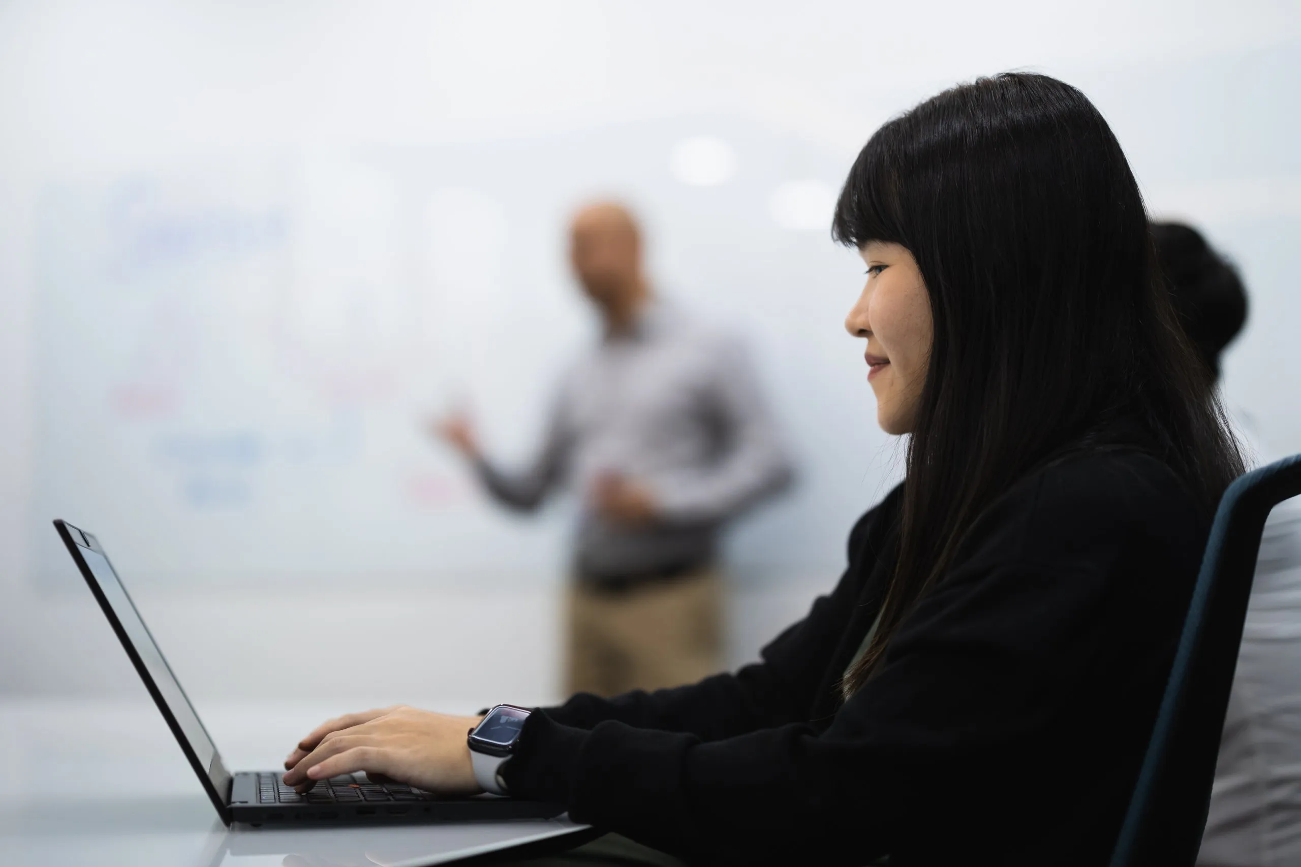 Woman working on a laptop in an office during a presentation.