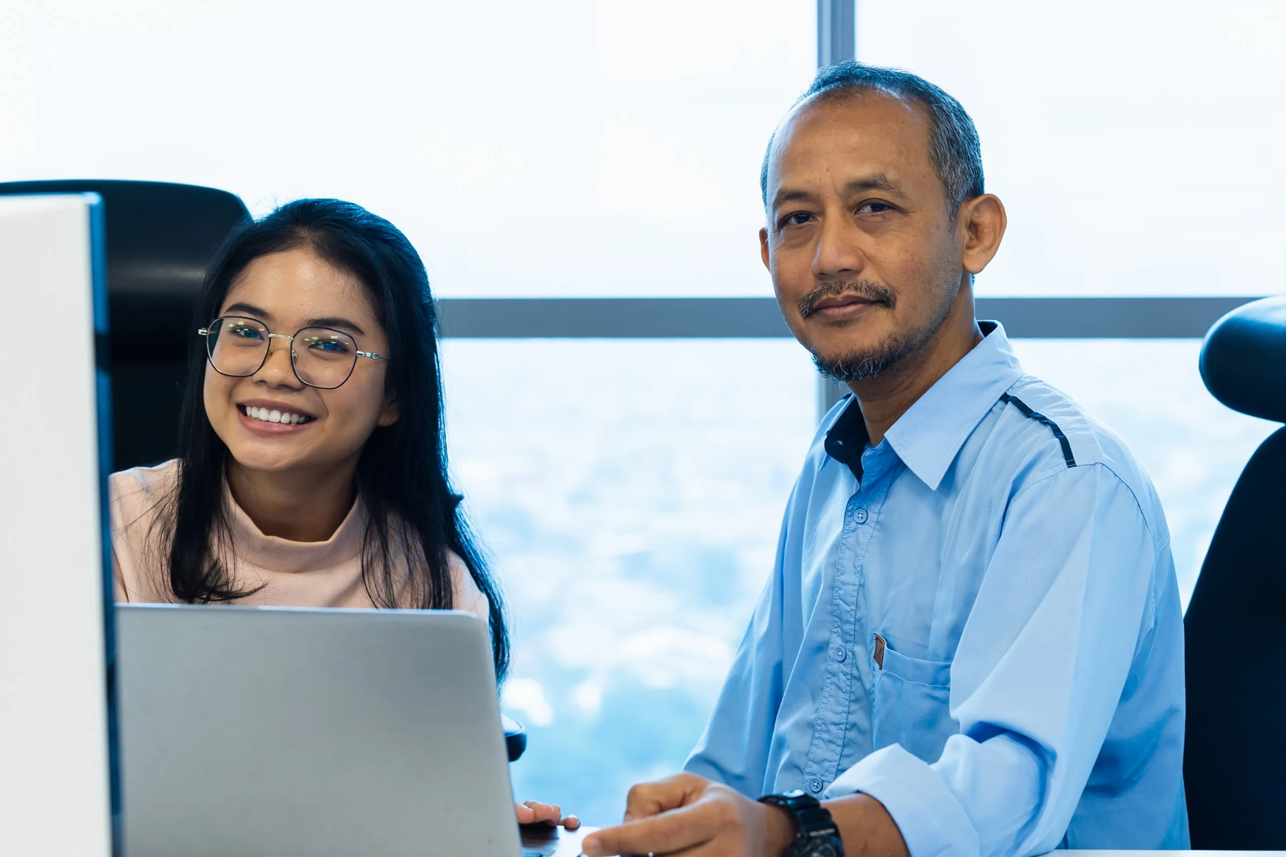 woman and man facing camera while working on computer in office setting.