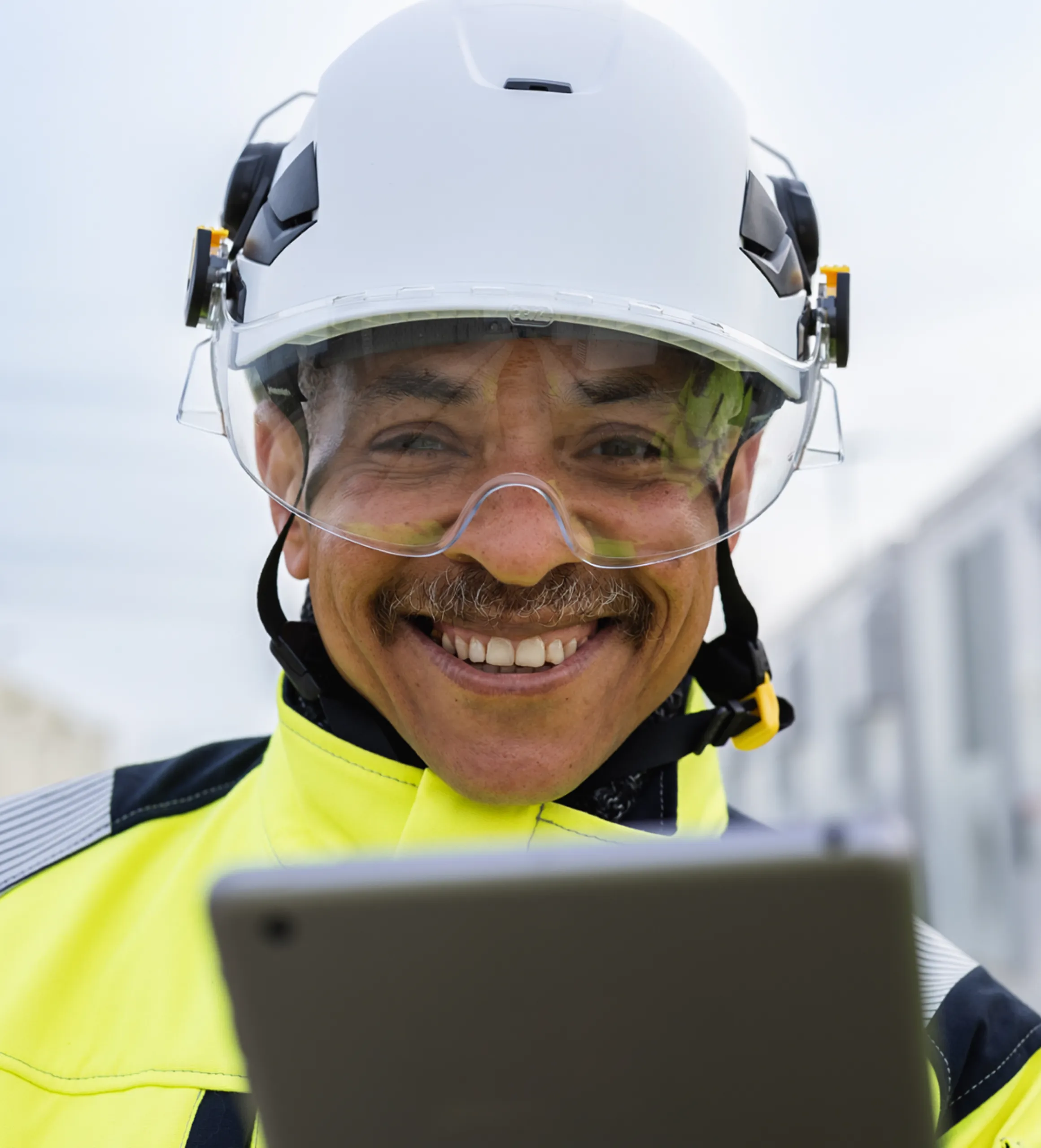 Technician in hard helmet and high visibility gear holding tablet.