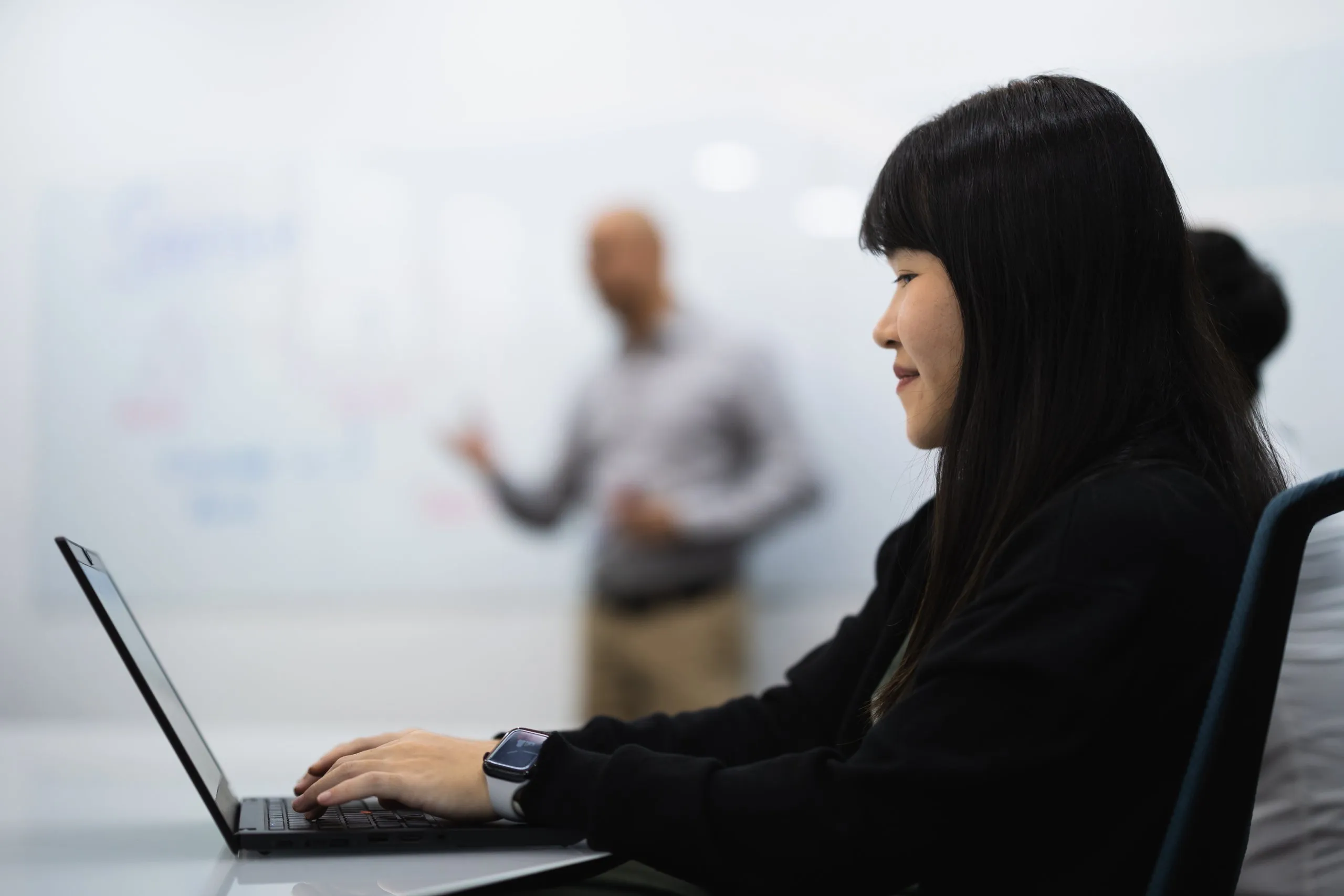 Woman working on a laptop in an office during a presentation.