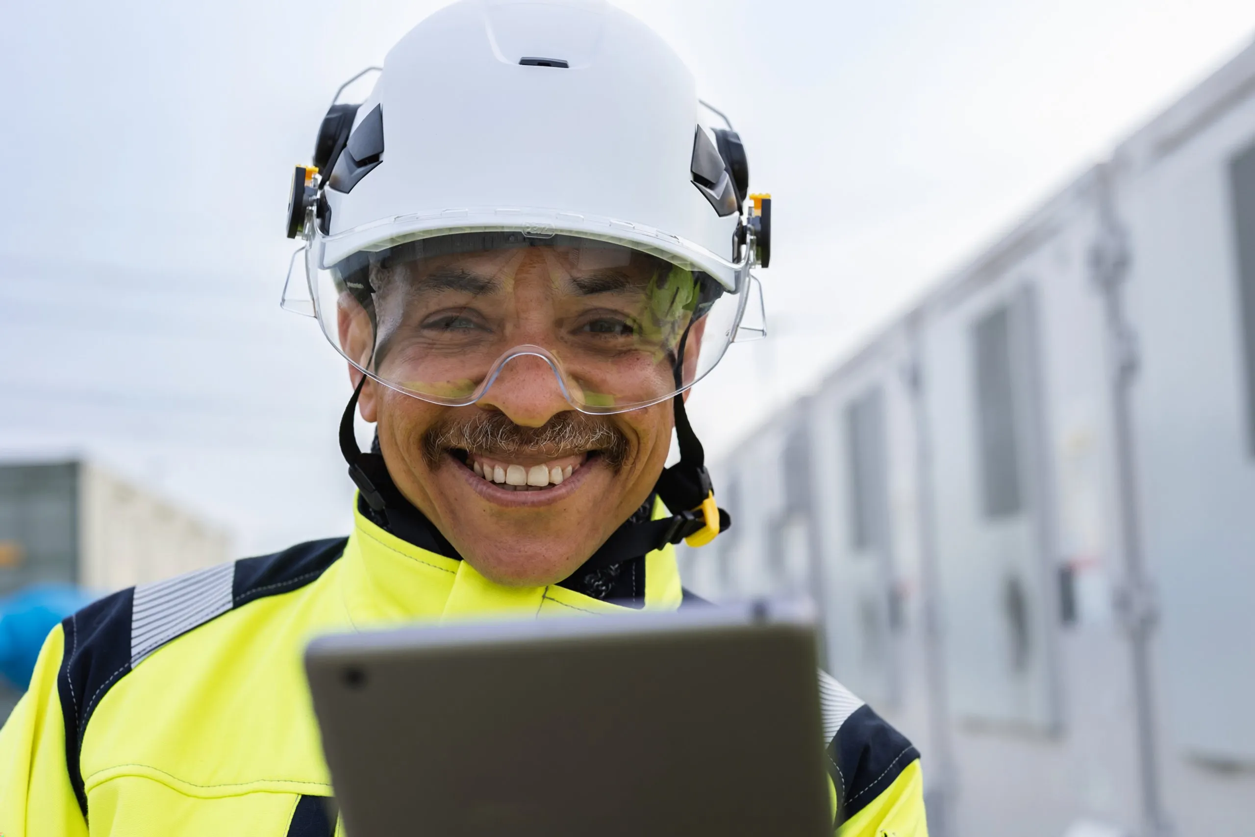Technician in hard helmet and high visibility gear holding tablet.