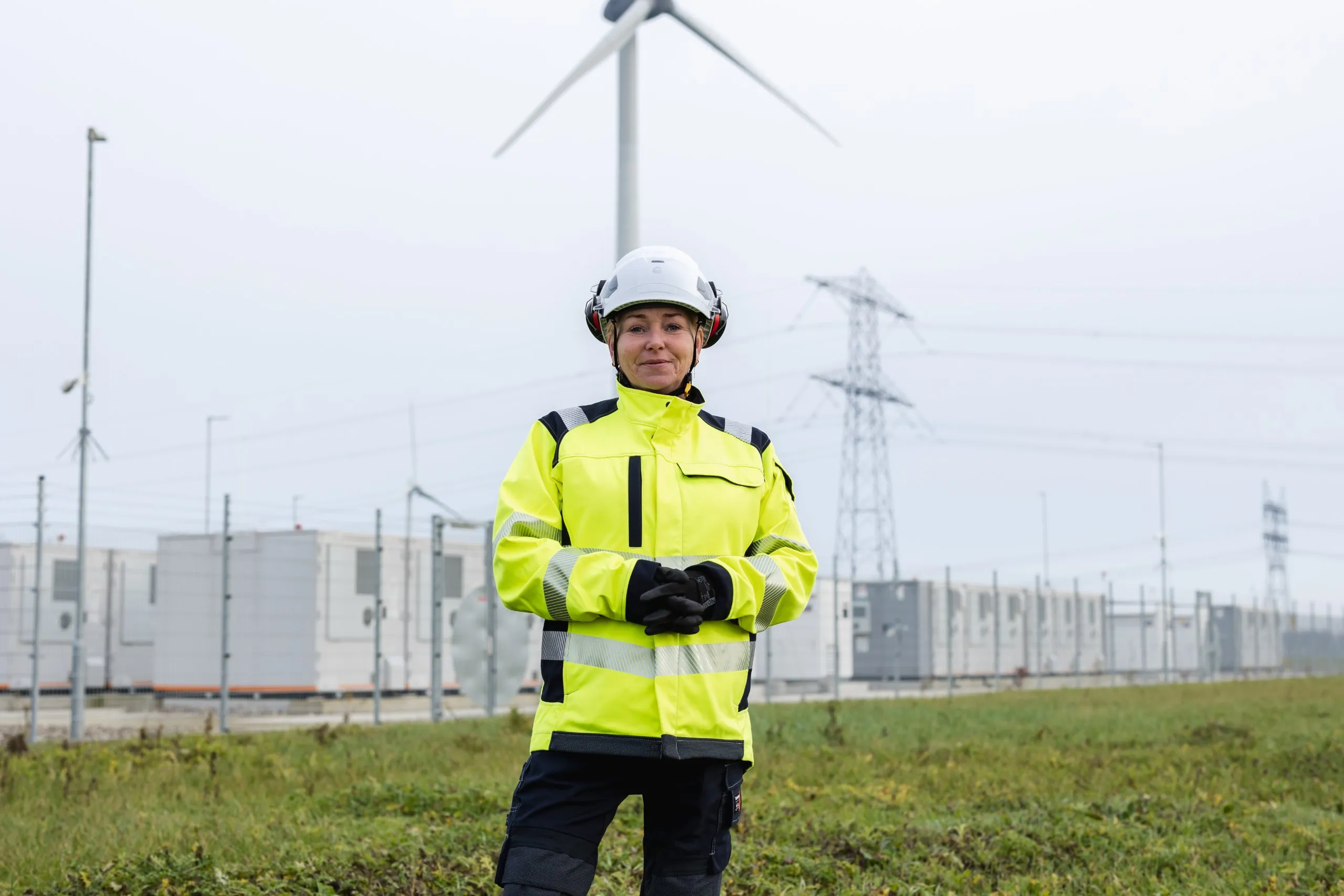 Technician in hard helmet and high visibility gear standing in front of energy storage untis.